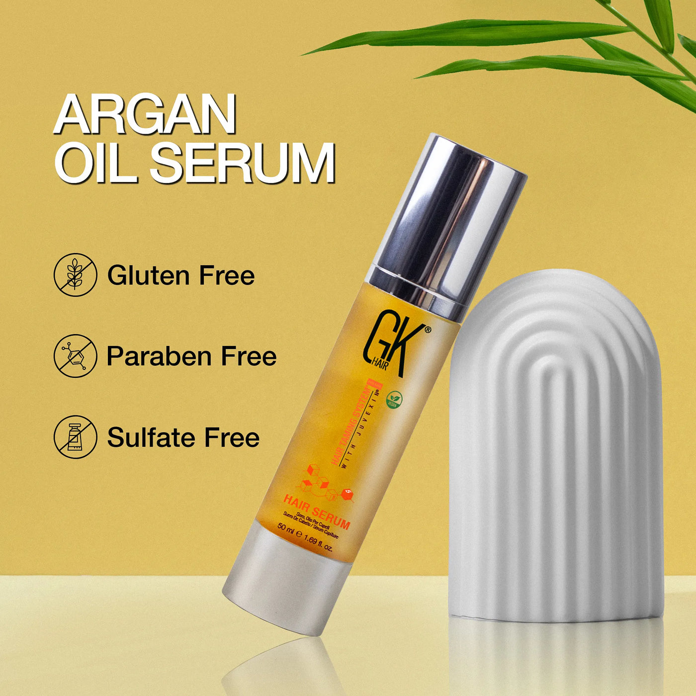 Argan oil serum bottle with silver cap on a yellow background. Text highlights features: gluten-free, paraben-free, sulfate-free. Green leaves accent.